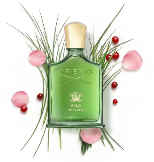 En grön parf bottle med guldlock omgiven av röda bär och rosa blomblad.