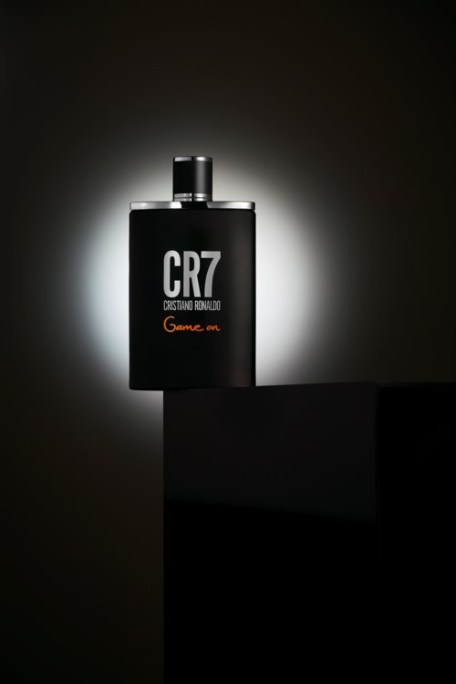 A perfume bottle with black color, white text "CR7" and "Cristiano Ronaldo", illuminated against a dark background.