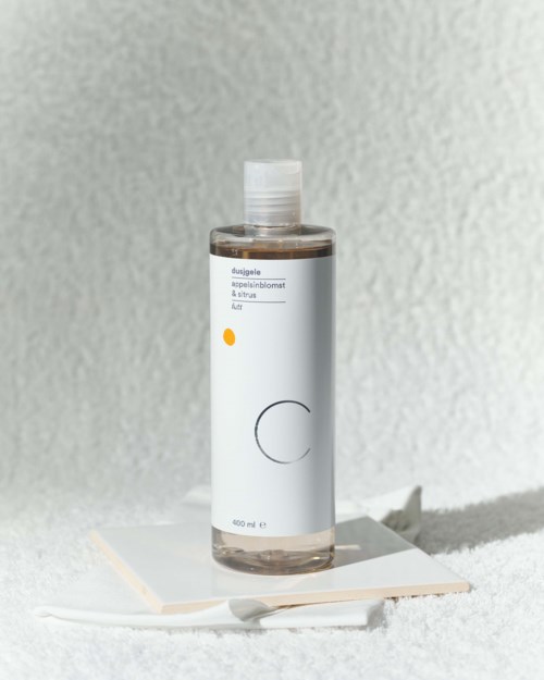 A transparent bottle with white label and clear cap on a white surface, sunlight shines on it.