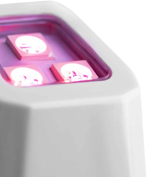 En apparat med rosa glödande lampor och små kvadratiska föremål inuti, kanske ett vetenskapligt eller laboratorieinstrument.