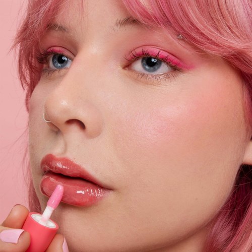 Een vrouw met roze haar brengt lipgloss aan.