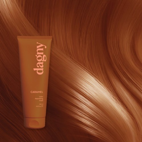 A tube labeled dagny caramel is placed against shiny, flowing caramel-colored hair.