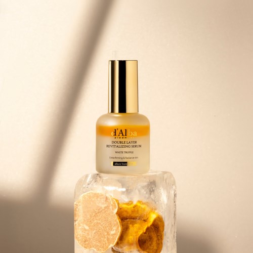 Ein Hautpflege-Serumflasche mit Goldkappe steht auf einem klaren Block, mit einer rosa Trockenblume und einer gelben getrockneten Blume.