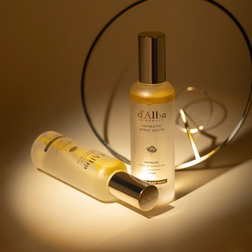 Zwei Flaschen Aromatic Spray Serum neben einem runden Spiegel mit warmem Licht.