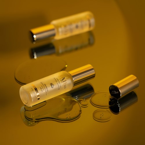 Ein Hautpflegeprodukt mit einer weißen Flasche und Metallverschluss, Flüssigkeit verschüttet auf einer reflektierenden Oberfläche.