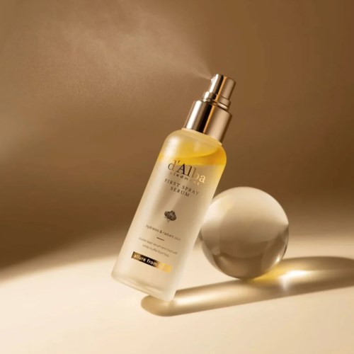 Eine Sprühflasche mit d'Aila First Spray Serum und gelber Flüssigkeit, neben einer runden weißen Kugel.