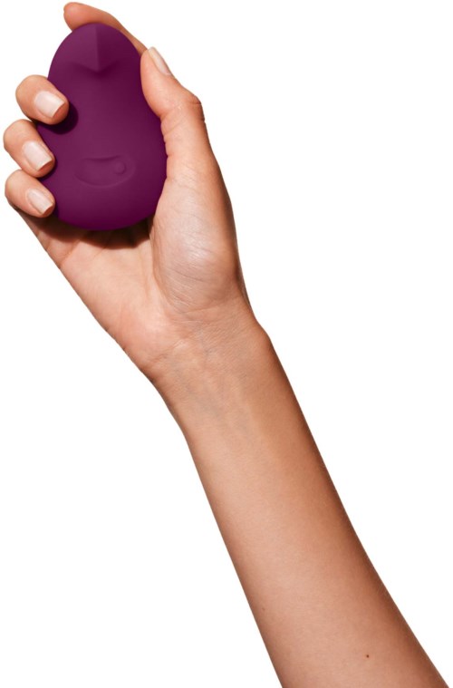 A hand holds a purple, egg-shaped object, gripping it firmly with fingers. The background is white.