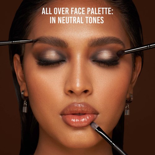 Makeup artists apply neutral-tone eyeshadow on woman's eyelids and lip gloss on lips.