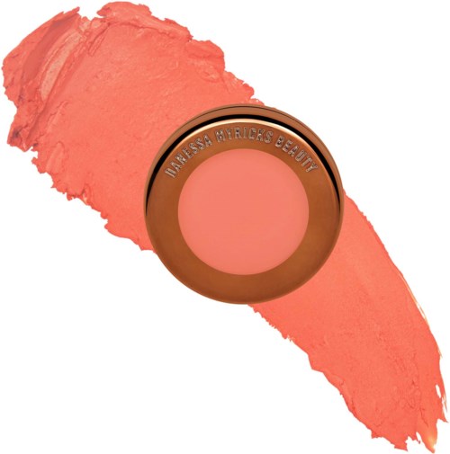 Round compact with pink blush, labeled Vanissa Byricks Beauty, on a pink streak. It appears to be makeup.