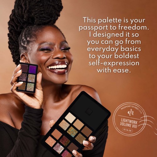 A smiling woman holding a colorful eyeshadow palette and a black makeup box with her hair in dreadlocks.