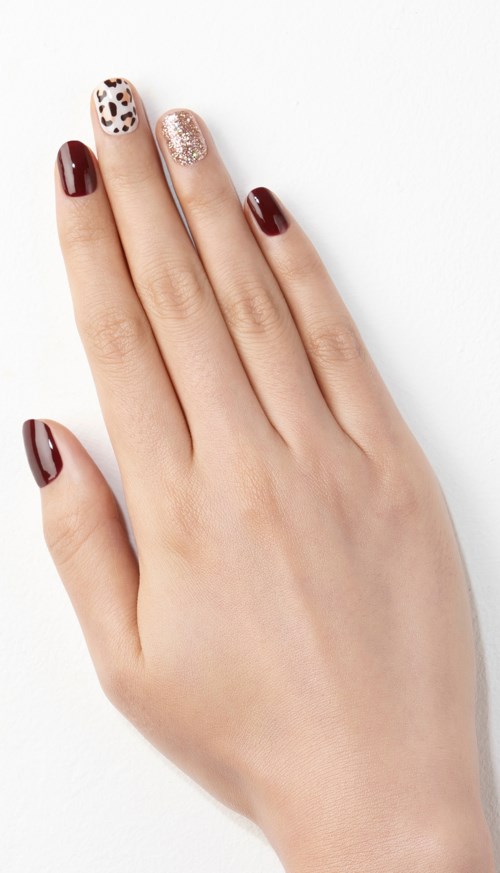 A hand with decorated nails, featuring dark red, leopard print, and glitter designs on three fingers.