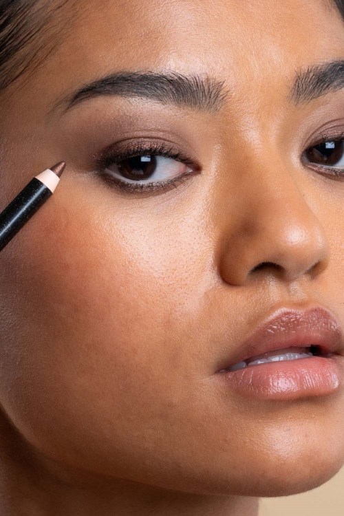 A woman applying eye makeup near her eyelid with a black eyeliner pencil.