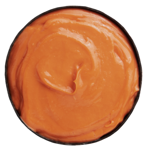 En rund behållare fylld med slät, orange färgad pålägg eller sås.