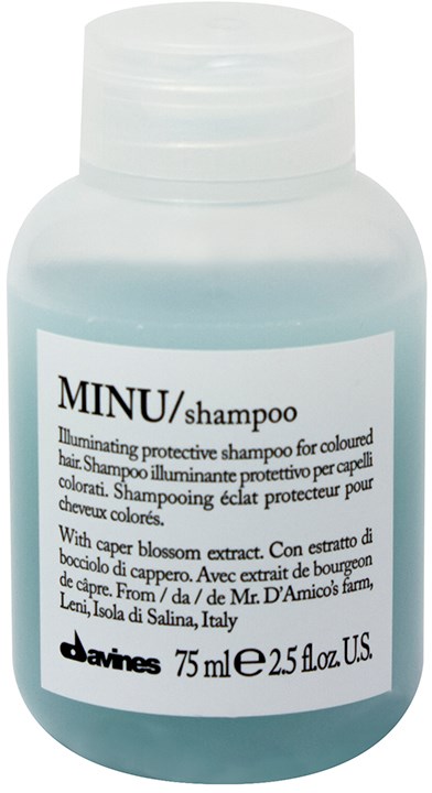 En lys blå flaske med shampoo med hvid etiket og hvid låg. Etiketten siger, at den er beskyttende og til farvet hår.