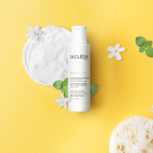 En vit flaska av Decléor Aroma Cleanse med vita och gröna blommor runt på en gul bakgrund.