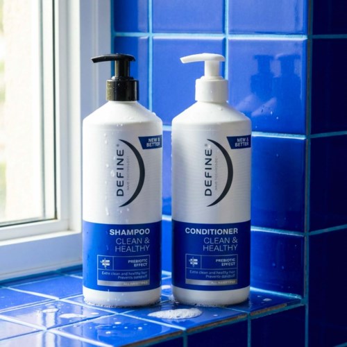 Two white bottles of shampoo and conditioner sit on a blue-tiled bathroom ledge by a window.