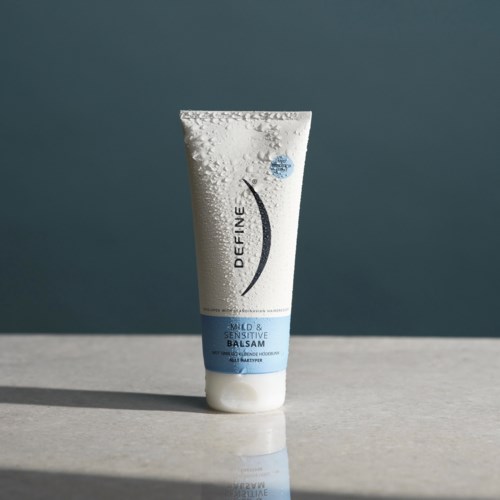 Hvit tube med hudkrem med blå etikett som sier 'Mild & Sensitive Balsam'.