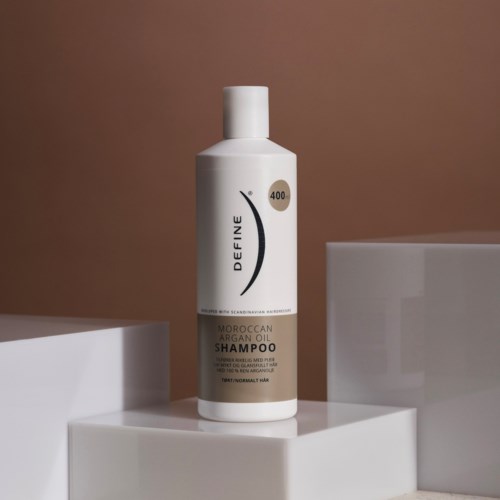 A white bottle of Moroccan Argan Oil shampoo with black and gold text on a white surface.