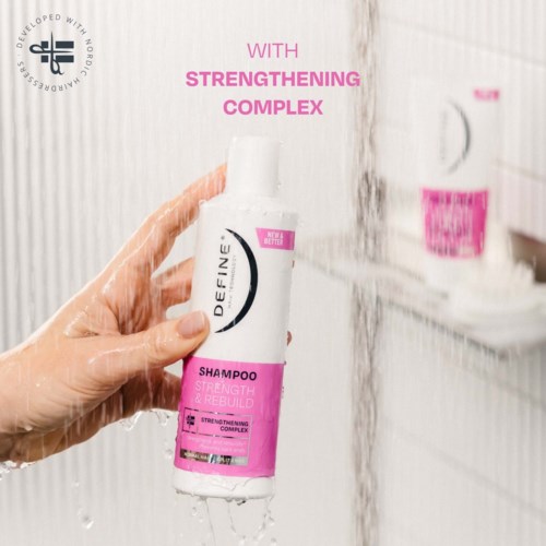 A hand holds a white and pink shampoo bottle with text about strengthening and rebuilding hair.