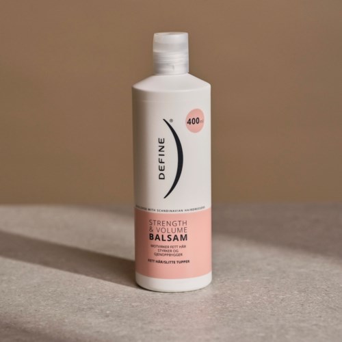 En hvit flaske med rosa og svart etikett, inneholder styrke og volum balsam for hår, står på en flat overflate.