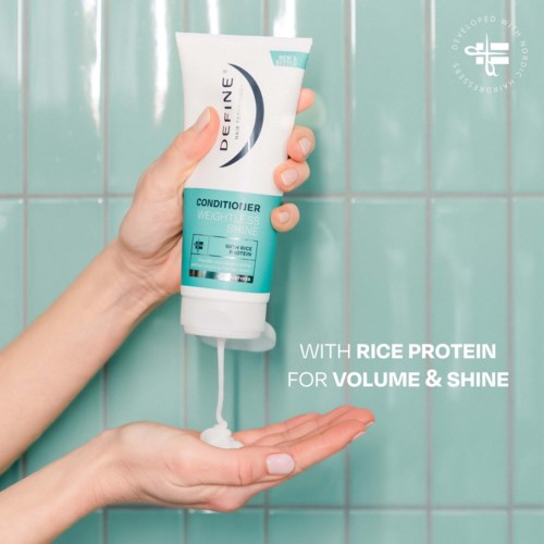 Een hand houdt een tube conditioner met rijstproteïne, voor volume en glans, tegen een betegelde badkamerwand.