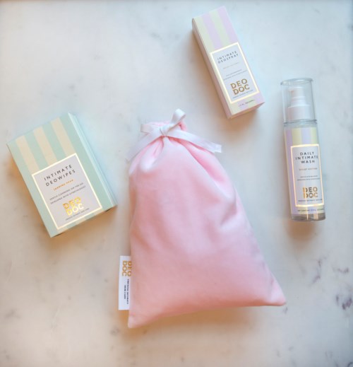 Tre hudpleieprodukter og en rosa stoffpose på en marmorflate.