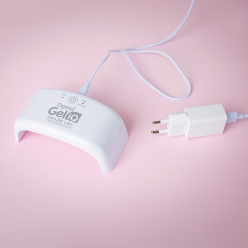A white device labeled 'Geliq' connected to a power plug on a pink background, used for UV nail curing.