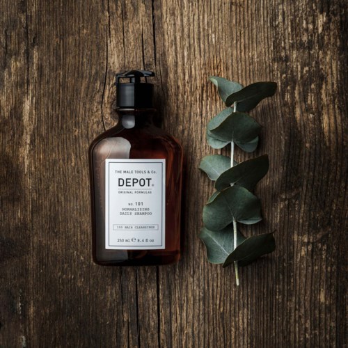 En brun shampoo-flaske med sort pumpe ligger på træoverflade ved siden af en eucalyptus-gren.