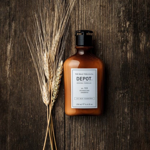 A brown shampoo bottle with a white label on a wooden surface, next to a wheat bundle and a small branch.