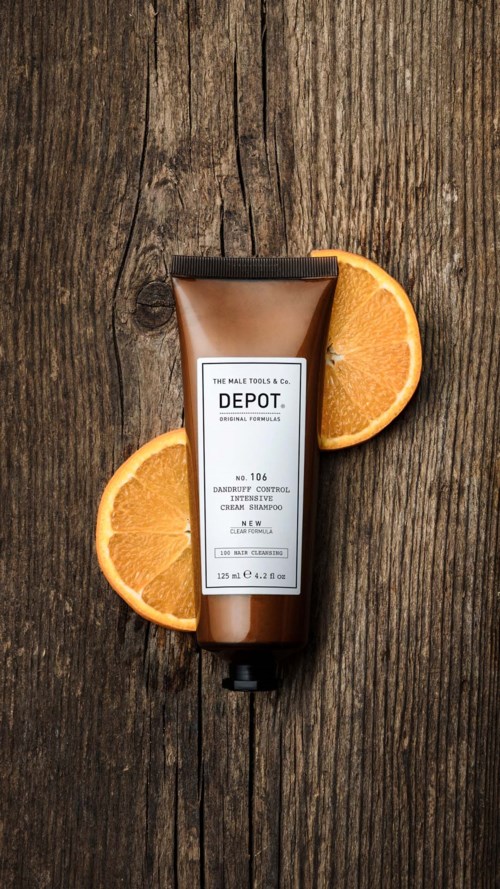En flaske skægshampoo på træ med appelsinskiver omkring den.