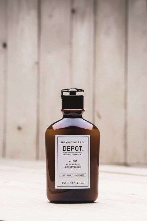 A brown bottle with a pump, labeled 'Depot' conditioning product, standing on a light wooden surface.
