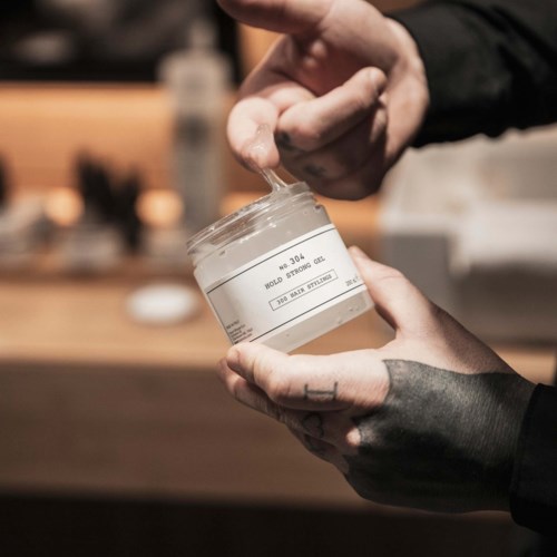Nogen holder et glas med creme eller lotion, mens den anden hånd dypper ud af det.