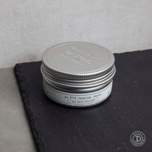 En rund silverfärgad behållare med hårstylingprodukt märkt 'Charcoal Paste' på en svart yta.