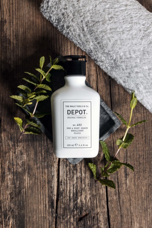 Een witte fles met label DEPOT ligt op een houten oppervlak naast een grijze handdoek en groene bladeren.