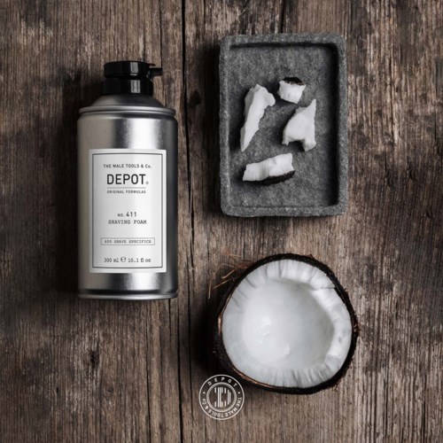 A bottle of shaving foam, a foam tray with torn paper, and a coconut on a wooden surface.