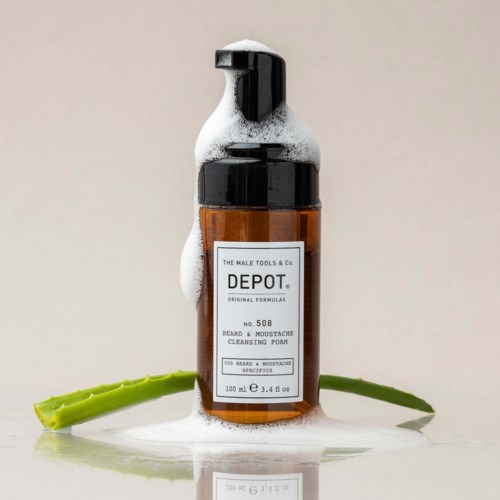 En brun flaske med svart pumpe, merket for skjegg og bart rens, omgitt av såpebobler og muligens aloe vera.