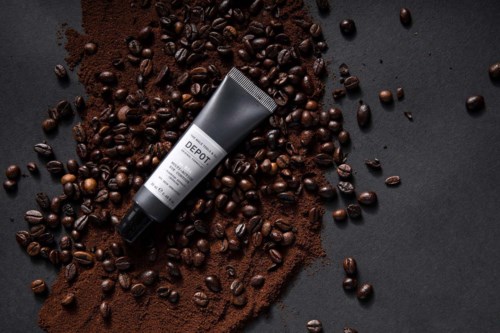 Et tubeprodukt ligger blant kaffebønner og malt kaffe på en mørk overflate.