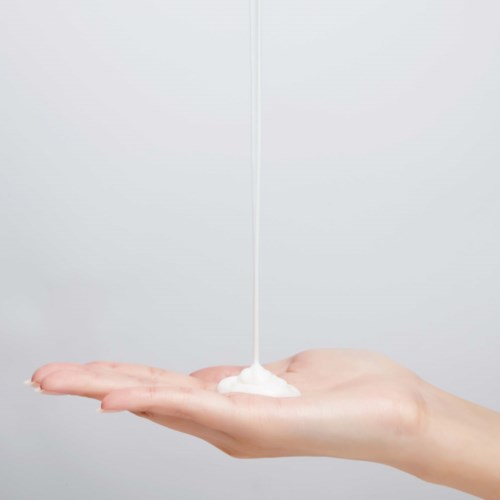 Een hand vangt witte lotion die van boven op de hand ligt.