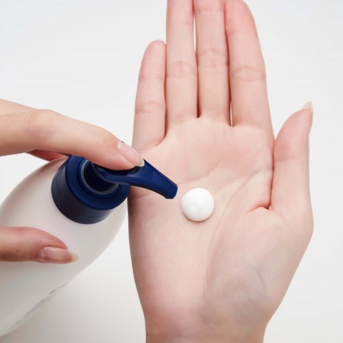 Iemand drukt witte crème uit een blauwe fles op zijn handpalm.