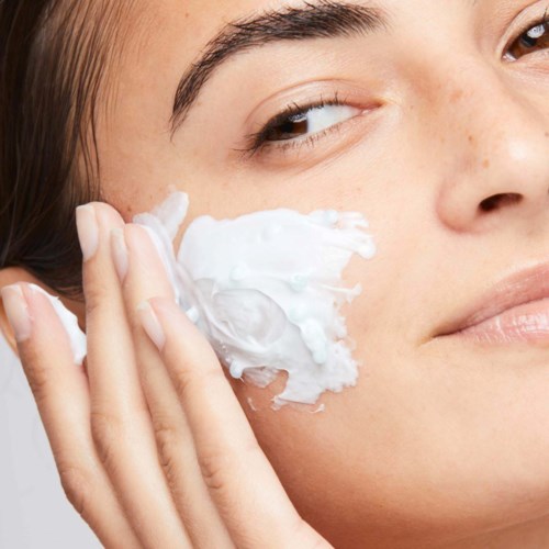 En flicka applicerar kräm på ansiktet, fokuserar på kinden, med tydlig hy och naturlig makeup.