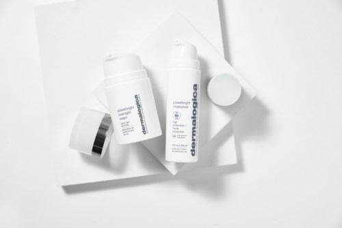 Dwie butelki produktów do pielęgnacji skóry z białymi nakrętkami na białej powierzchni, jedna oznaczona 'dermadiolabe' i 'powerful moisture.'