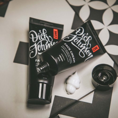 Two black tubes of Dick Johnson face cream are on black and white checkered background with some foam.