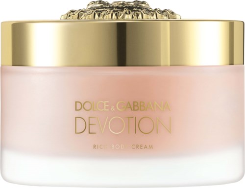 En rosa kroppskremkrukke med gullhette og en klar dekorativ topp, merket Dolce & Gabbana Devotion.