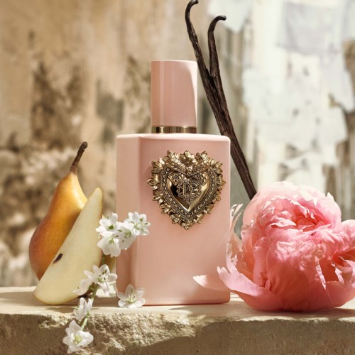 Een roze parfumfles met een decoratief hart, omgeven door peer, vaniljebloem, kersenbloesem en vanillevaten.