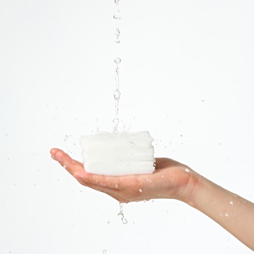 Eine Hand hält einen Stapel weiße Seife mit fallenden Wassertropfen.