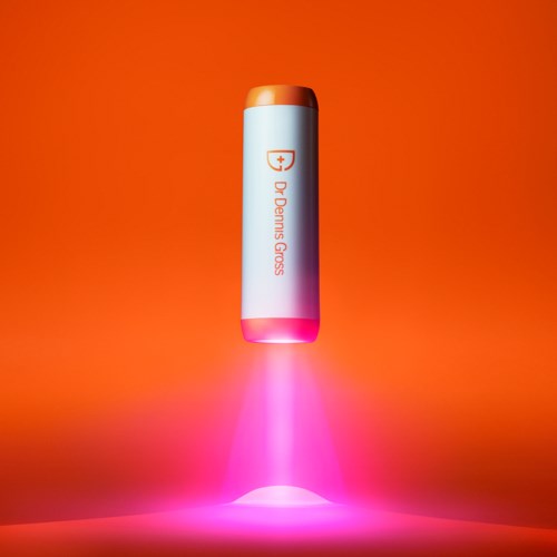 Et hvitt batteri med logo og tekst, som gløder rosa og svever over en rosa overflate med oransje bakgrunn.