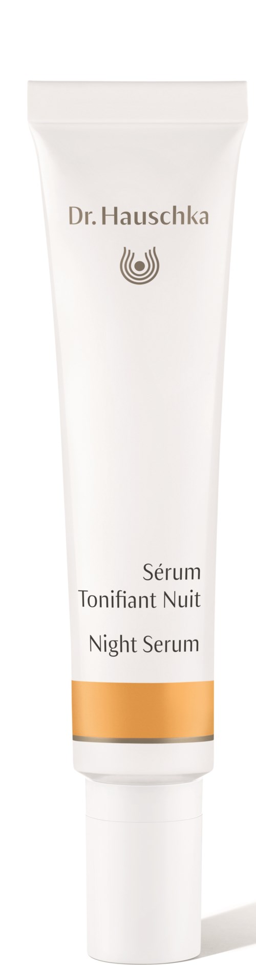 A white tube of night serum with gold accents has the brand name 'Dr. Hauschka' and product name in multiple languages.