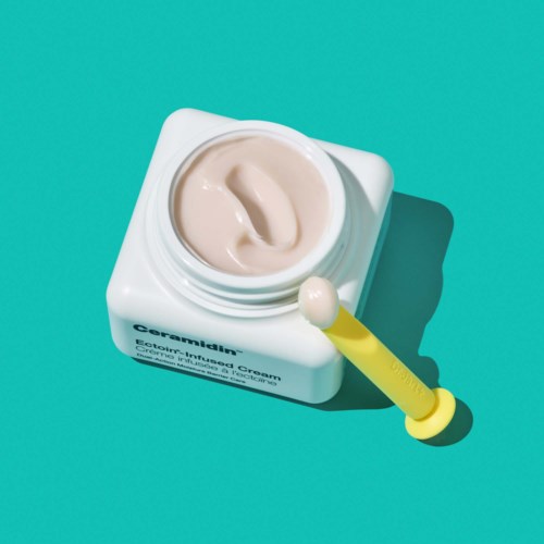 A jar of cream with a yellow applicator on a turquoise background.