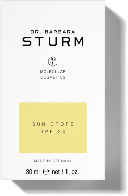 Białe opakowanie kosmetyków skórnych z czarnym tekstem, żółtą naklejką i prostym designem. Reklamuje krople słoneczne SPF 30 z Niemiec.
