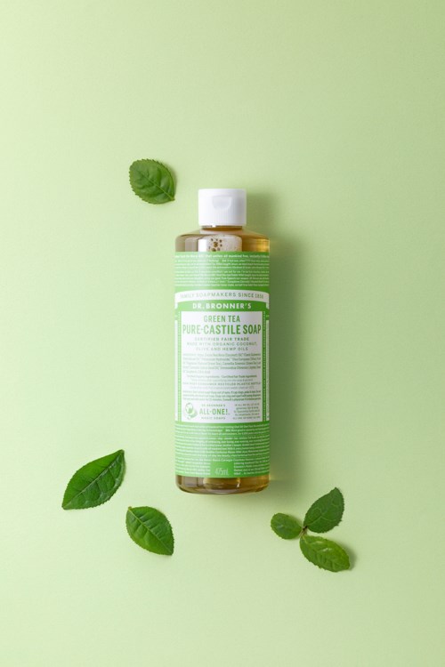 En grön flaska med tea tree castile tvål med fyra tea leaves runt den på en grön bakgrund.